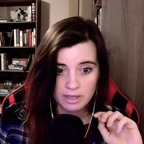 A Woman Wearing Headphones And A Plaid Shirt Is Talking Into A Microphone In Front Of A Bookshelf GIF