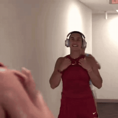 A Woman Wearing Headphones And A Red Nike Shirt Is Smiling GIF