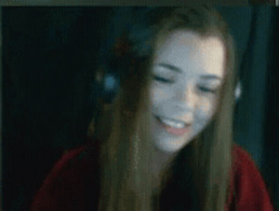 A Woman Wearing Headphones And A Red Shirt Is Smiling While Sitting In Front Of A Computer Screen . GIF