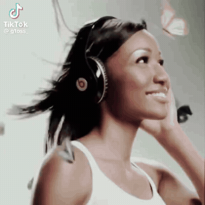 A Woman Wearing Headphones And A White Tank Top Is Smiling . GIF