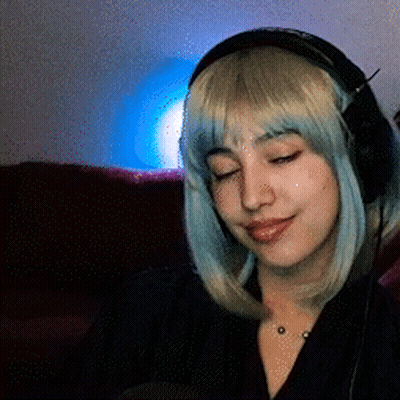 A Woman Wearing Headphones And A Wig Is Sitting On A Couch GIF