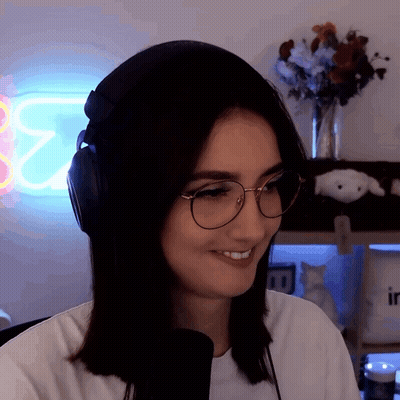 A Woman Wearing Headphones And Glasses Smiles In Front Of A Neon Sign That Says ' E2 ' GIF