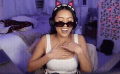 A Woman Wearing Headphones And Sunglasses Is Sitting On A Bed . GIF