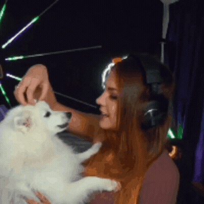 A Woman Wearing Headphones Holds A Small White Dog GIF
