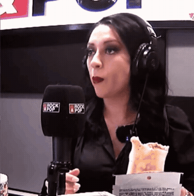 A Woman Wearing Headphones Is Eating A Taco In Front Of A Microphone That Says Rock & Pop GIF