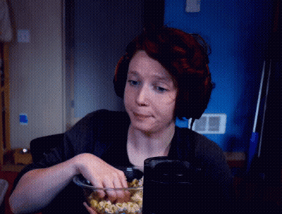 A Woman Wearing Headphones Is Eating Popcorn In Front Of A Blue Wall GIF