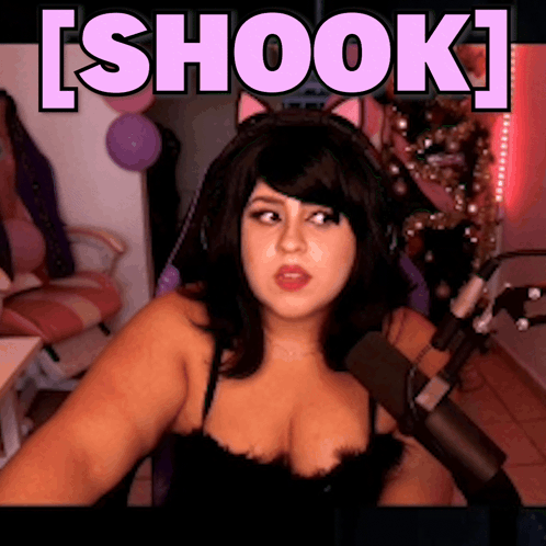 A Woman Wearing Headphones Is Sitting In Front Of A Microphone With The Word Shook Above Her GIF
