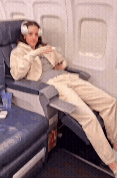 A Woman Wearing Headphones Is Sitting On A Plane . GIF