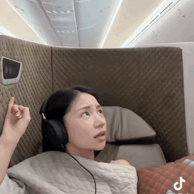 A Woman Wearing Headphones Is Sitting On An Airplane GIF