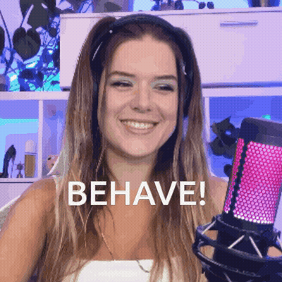 A Woman Wearing Headphones Is Smiling And Holding A Microphone With The Word Behave Written On It GIF