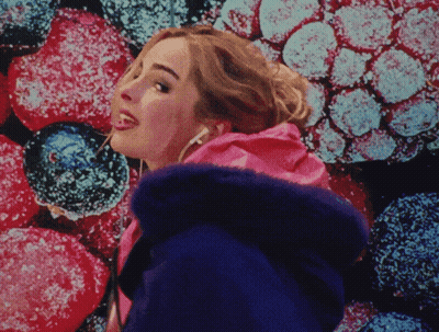 A Woman Wearing Headphones Is Standing In Front Of A Colorful Background Of Berries GIF