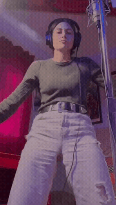 A Woman Wearing Headphones Is Standing In Front Of A Microphone . GIF