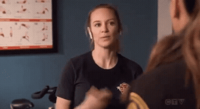 A Woman Wearing Headphones Is Talking To A Man In A Gym While Sitting On An Exercise Bike . GIF