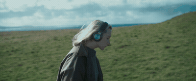 A Woman Wearing Headphones Is Walking Through A Field GIF