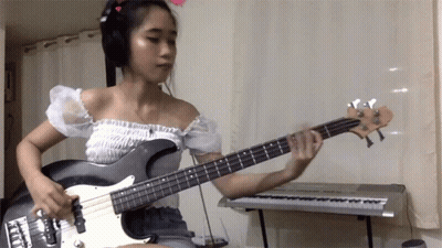 A Woman Wearing Headphones Plays A Bass Guitar GIF