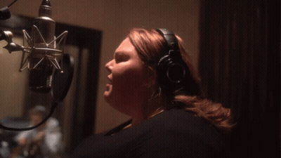 A Woman Wearing Headphones Sings Into A Microphone In A Dark Room GIF