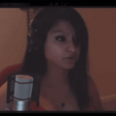 A Woman Wearing Headphones Stands In Front Of A Microphone And Looks At The Camera GIF