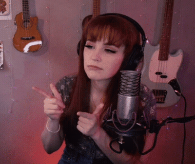 A Woman Wearing Headphones Stands In Front Of A Microphone With Guitars Behind Her GIF