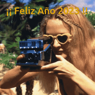 A Woman Wearing Heart Shaped Sunglasses Is Taking A Picture With A Polaroid Camera With The Words Feliz Ano 2023 Written GIF