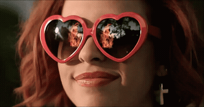 A Woman Wearing Heart Shaped Sunglasses With A Reflection Of Fire GIF