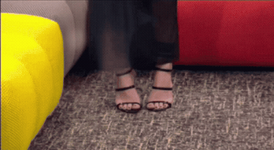 A Woman Wearing High Heels Is Standing In Front Of A Red Couch GIF