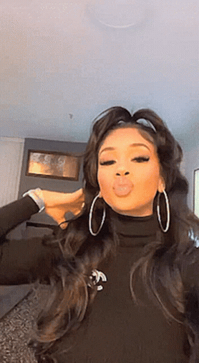A Woman Wearing Hoop Earrings And A Black Turtleneck Is Making A Funny Face . GIF
