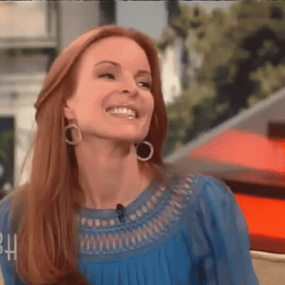 A Woman Wearing Hoop Earrings And A Blue Top Smiles GIF