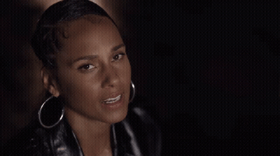 A Woman Wearing Hoop Earrings And A Leather Jacket Looks At The Camera . GIF
