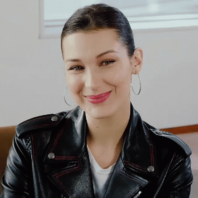 A Woman Wearing Hoop Earrings And A Leather Jacket Smiles GIF