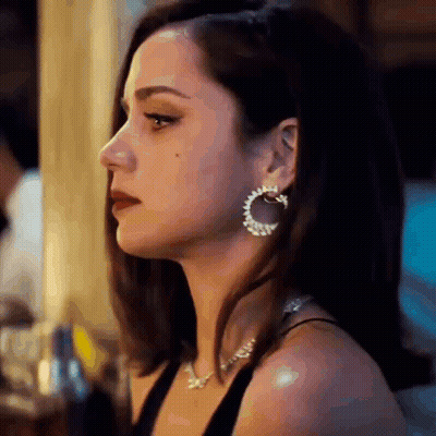 A Woman Wearing Hoop Earrings And A Necklace Is Looking Down . GIF