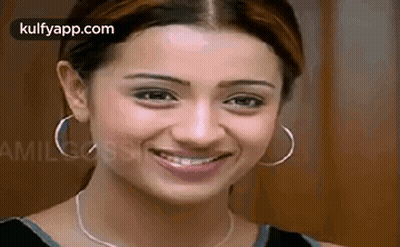 A Woman Wearing Hoop Earrings And A Necklace Is Smiling For The Camera . GIF