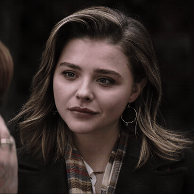 A Woman Wearing Hoop Earrings And A Plaid Scarf Looks At The Camera GIF