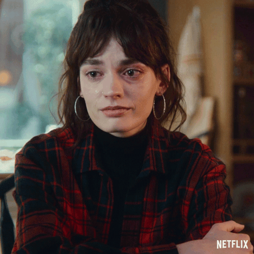 A Woman Wearing Hoop Earrings And A Plaid Shirt With Netflix Written On The Bottom Right GIF