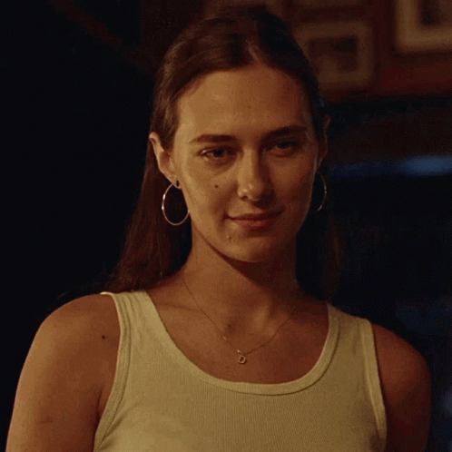 A Woman Wearing Hoop Earrings And A Tank Top Looks At The Camera GIF