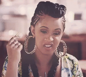 A Woman Wearing Hoop Earrings And Braids Is Sitting At A Table With A Drink In Her Hand . GIF