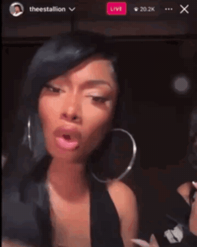 A Woman Wearing Hoop Earrings Is Making A Funny Face In Front Of A Live Audience GIF