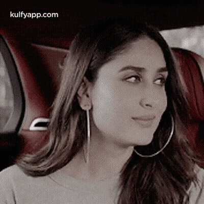 A Woman Wearing Hoop Earrings Is Sitting In A Car And Looking At The Camera . GIF