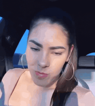 A Woman Wearing Hoop Earrings Is Sitting In A Car And Making A Funny Face GIF