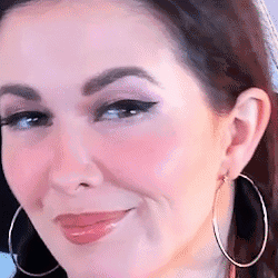 A Woman Wearing Hoop Earrings Is Smiling And Looking At The Camera . GIF