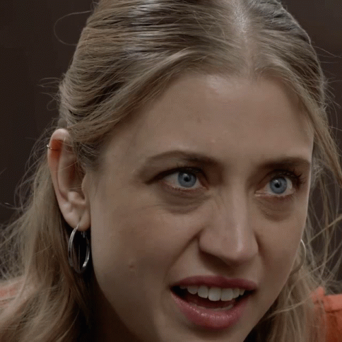 A Woman Wearing Hoop Earrings Is Smiling With Her Mouth Wide Open GIF