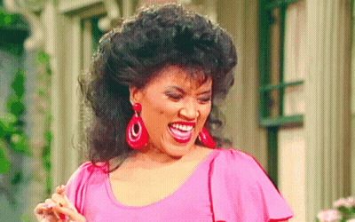 A Woman Wearing Red Earrings And A Pink Shirt Is Smiling GIF