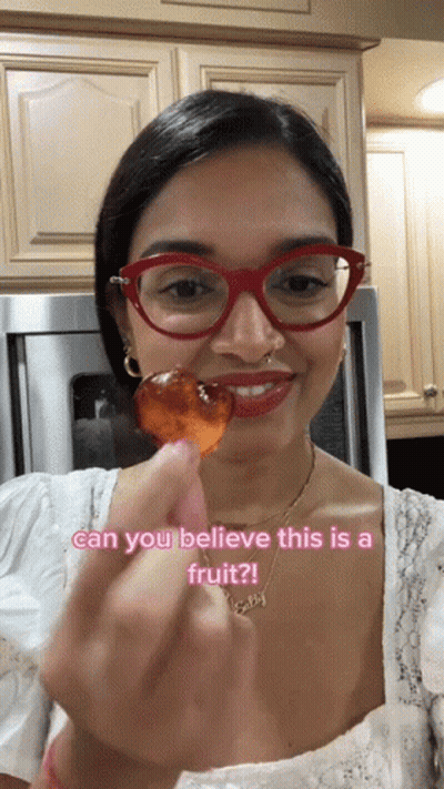 A Woman Wearing Red Glasses Is Holding A Piece Of Fruit With The Caption Can You Believe This Is A Fruit ? GIF