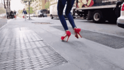A Woman Wearing Red High Heels Crosses A Street GIF