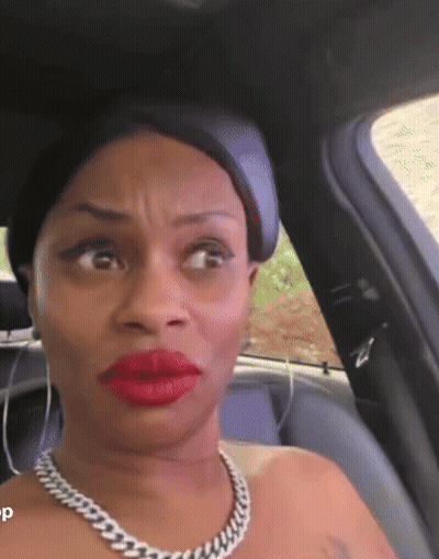 A Woman Wearing Red Lipstick And A Chain Necklace Is Sitting In A Car . GIF