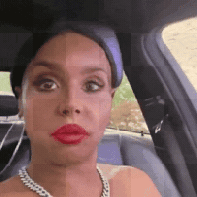 A Woman Wearing Red Lipstick And A Chain Necklace Is Sitting In A Car GIF