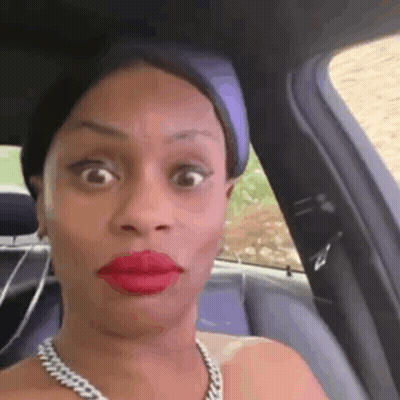 A Woman Wearing Red Lipstick And A Necklace Is Sitting In The Back Seat Of A Car Making A Funny Face . GIF