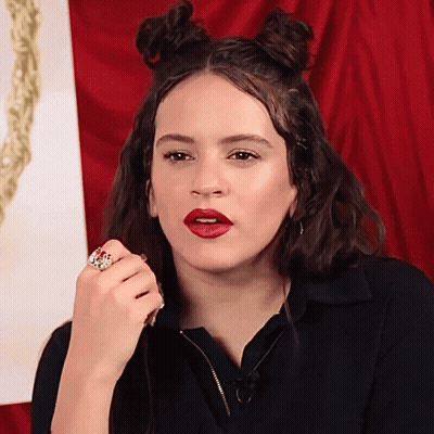 A Woman Wearing Red Lipstick And A Ring On Her Finger Looks At The Camera GIF