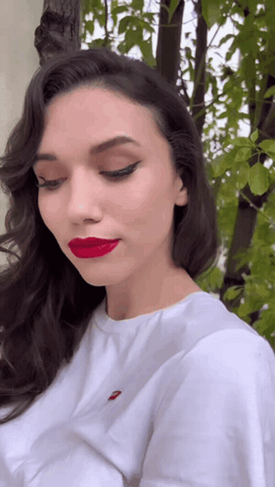 A Woman Wearing Red Lipstick And A White Shirt With A Red Embroidered Levis Logo On It GIF