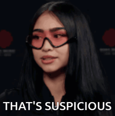 A Woman Wearing Red Sunglasses And A Black Jacket Is Saying That 'S Suspicious . GIF
