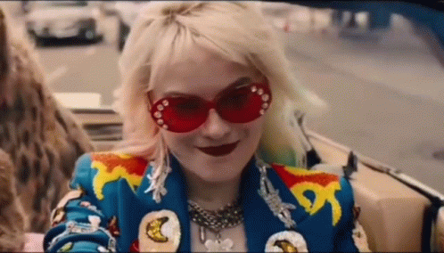 A Woman Wearing Red Sunglasses And A Blue Jacket Is Sitting In A Convertible Car . GIF